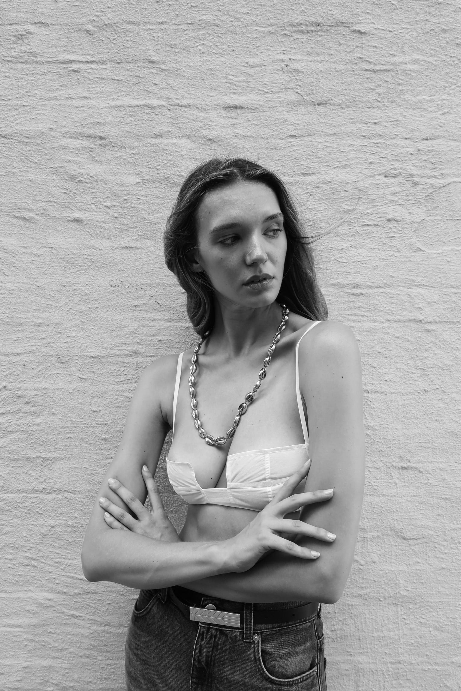 Long silver concha puka necklace by Tohum on model against a brick wall from Blackbird Collection's sustainable accessories and jewelry